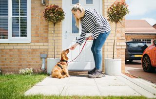 A side-view shot of a caucasian woman giving her dog a treat outside her house, they are about to go on a walk.